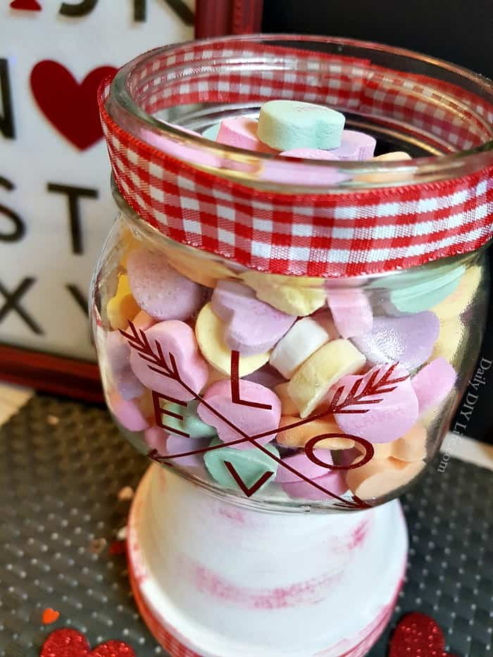 Fill up this incredibly simple Mason Jar Valentine Candy Dish with your favorite sweets for your sweetie. Who doesn't love a little something extra sweet on Valentine's day? With just a few simple supplies you can put together this adorable, fun, candy dish as a gift for your honey, or just an extra addition to your holiday decor. #CricutMade #Cricut #MasonJarCrafts #ValentineCrafts #MasonJarValentine #VinylCrafts