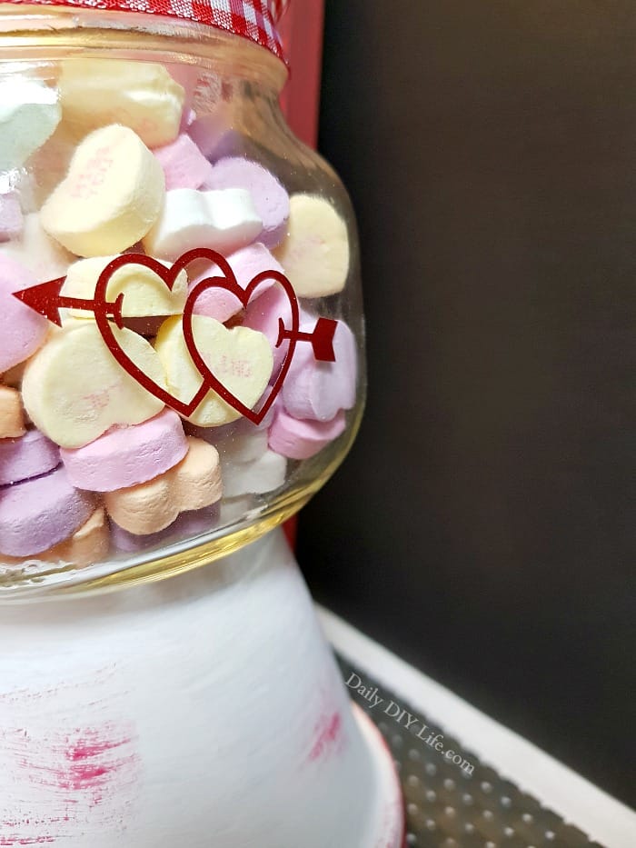 Fill up this incredibly simple Mason Jar Valentine Candy Dish with your favorite sweets for your sweetie. Who doesn't love a little something extra sweet on Valentine's day? With just a few simple supplies you can put together this adorable, fun, candy dish as a gift for your honey, or just an extra addition to your holiday decor. #CricutMade #Cricut #MasonJarCrafts #ValentineCrafts #MasonJarValentine #VinylCrafts