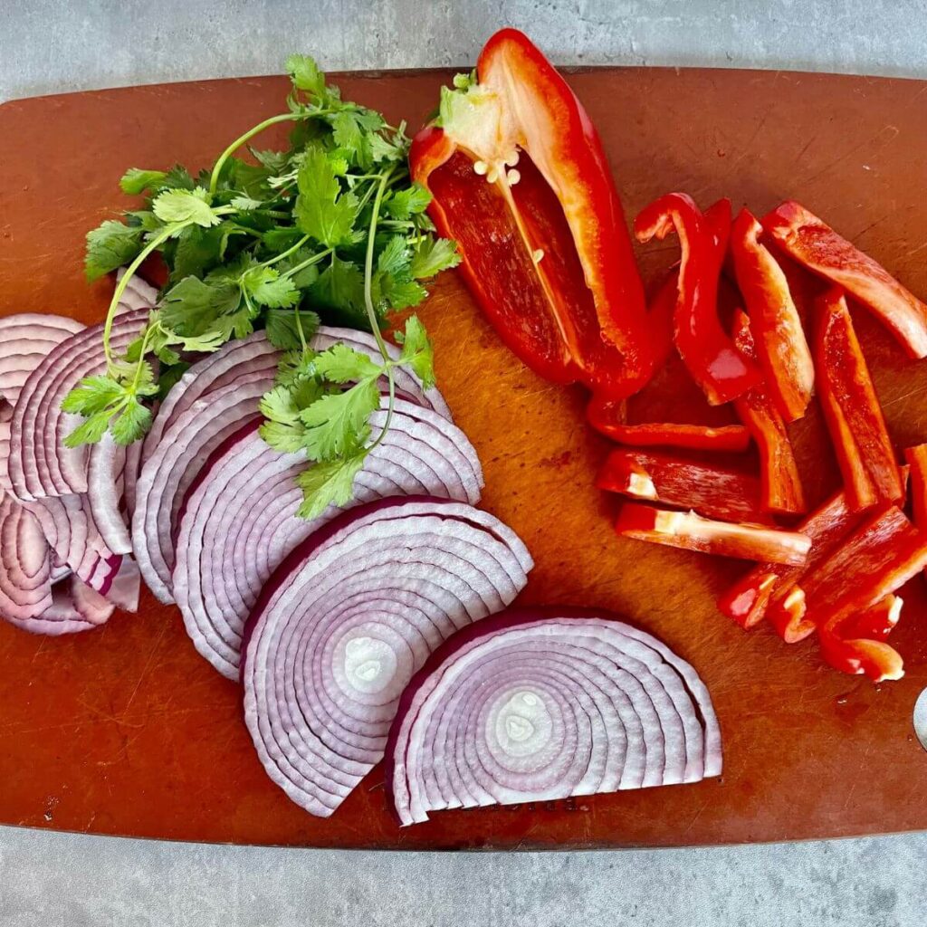 red onions and red bell peppers with cilantro on cutting board