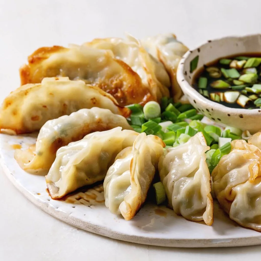 plate of dumplings with dip sauce and scallions